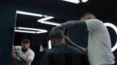 Açık boğazlı, keskin tıraş bıçaklı profesyonel berber erkek şakaklarında saç tıraşı olur. Çekici erkek berber dükkanında modern bir saç kesimi yaptırıyor. Yakın çekim. El kamerasıyla. 4K.