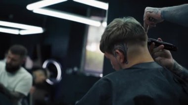Elektrikli traşlı erkek saç kesimi. Saç kesme stilini kapat. Berber, berber dükkanında saç kesme makinesi kullanarak müşterisinin saçını kesiyor. Elektrikli traşlı erkek kuaförü. El kamerasıyla. 4K.