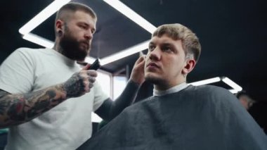 Elektrikli traşlı erkek saç kesimi. Saç kesme stilini kapat. Berber, berber dükkanında saç kesme makinesi kullanarak müşterisinin saçını kesiyor. Elektrikli traşlı erkek kuaförü. El kamerasıyla. 4K.