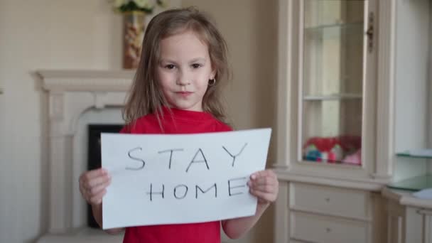 Fique em casa conceito. Menina pequena em vermelho T-shirt segurando sinal dizendo ficar em casa para proteção do vírus e cuidar de sua saúde de COVID-19 . — Vídeo de Stock