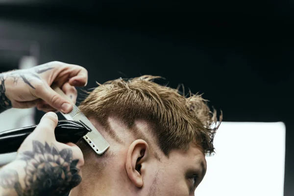 Männlicher Haarschnitt mit Rasiermesser. Tätowierte Friseurin schneidet Klienten im Friseursalon mit Haarschneidemaschine. Mann frisiert mit Elektrorasierer. — Stockfoto