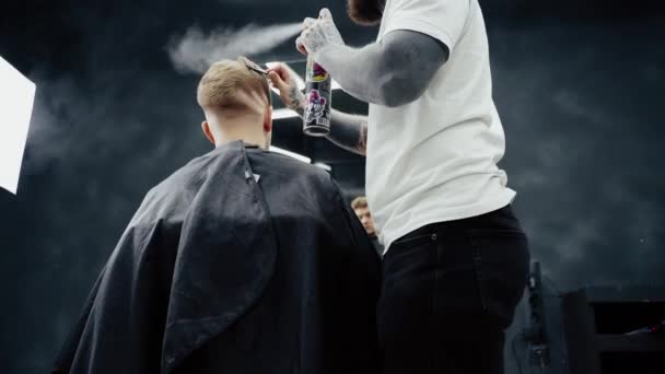 Kadeřník dělá účes se sprejem na vlasy po sestřihu v holičství. Mladý pohledný kavkazský muž dostat sestřih v moderním kadeřnictví. — Stock video