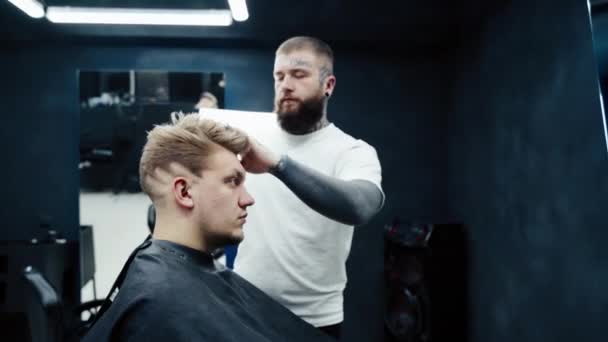 Peluquero hace el peinado con spray para el cabello después de corte de pelo en la peluquería. Joven guapo caucásico hombre consiguiendo un corte de pelo en un moderno salón de belleza . — Vídeo de stock