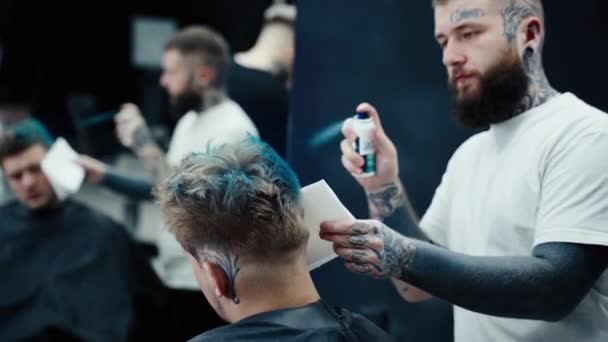 Hombre atractivo está consiguiendo un corte de pelo moderno en la peluquería. Peluquero tiñe el cabello al cliente con un spray azul . — Vídeos de Stock