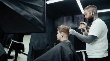 Berber kuaförde saç kesiminden sonra saç spreyi ile saç stili yapıyor. Genç yakışıklı beyaz adam modern bir kuaförde saçını kestiriyor..