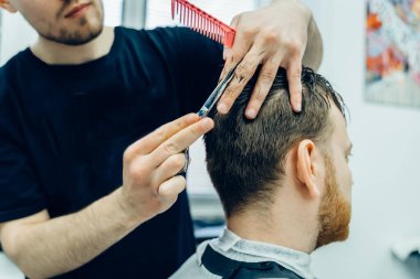 Dövmeli berber müşterinin saçını makasla kesiyor. Kapatın. Çekici erkek berber dükkanında modern bir saç kesimi yaptırıyor. Görüntüyü kapat.