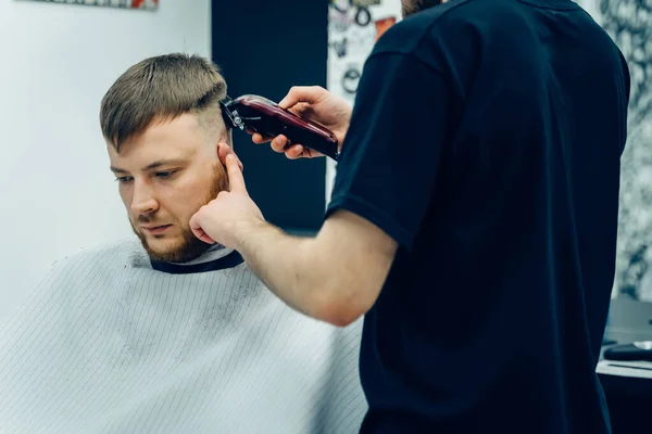 Male haircut with electric razor. Barber makes haircut for client at the barber shop by using hairclipper. Man hairdressing with electric shaver.