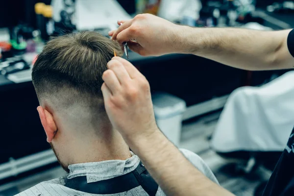 Tätowierter Barbier schneidet dem Kunden mit einer Schere die Haare. Aus nächster Nähe. Attraktive Männer bekommen im Friseursalon einen modernen Haarschnitt. Nahsicht. — Stockfoto