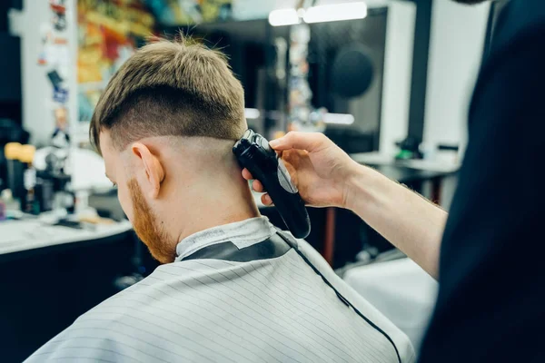 Männlicher Haarschnitt mit Rasiermesser. Friseur schneidet Kunden im Friseursalon mit Haarschneidemaschine. Mann frisiert mit Elektrorasierer. — Stockfoto