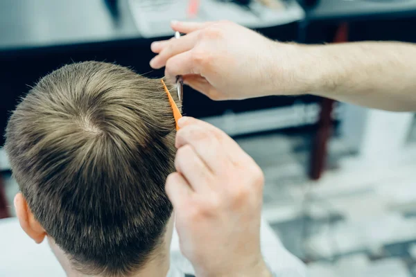 Tattooed Barber cuts the hair of the client with scissors. Close up. Attractive male is getting a modern haircut in barber shop. Close up view. — Stock Photo, Image