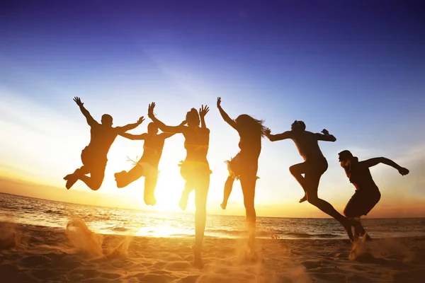 Amigos felices saltan al atardecer en la playa. Concepto de amistad o equipo — Foto de Stock