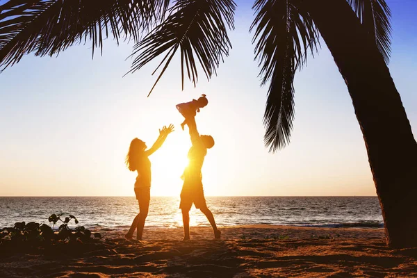 Felice famiglia divertendosi sotto le palme sulla spiaggia del tramonto — Foto Stock