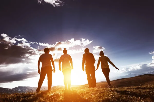 Quatro amigos ao pôr-do-sol fundo na cordilheira — Fotografia de Stock