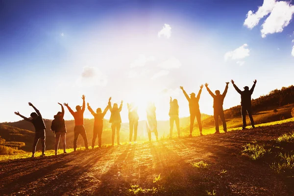 Grande grupo de amigos levantando os braços no pôr do sol juntos — Fotografia de Stock