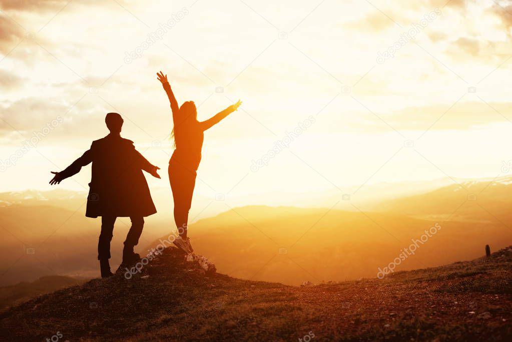 Happy couple raised arms sunset mountain
