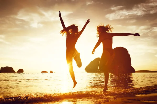 Twee gelukkige meisjes zonsondergang strand lopen-stap-springen — Stockfoto