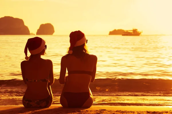 Две дамы в рождественских кепках на пляже на закате — стоковое фото