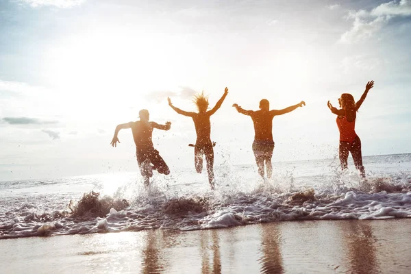 Quatre amis heureux courent à la plage du coucher du soleil — Photo