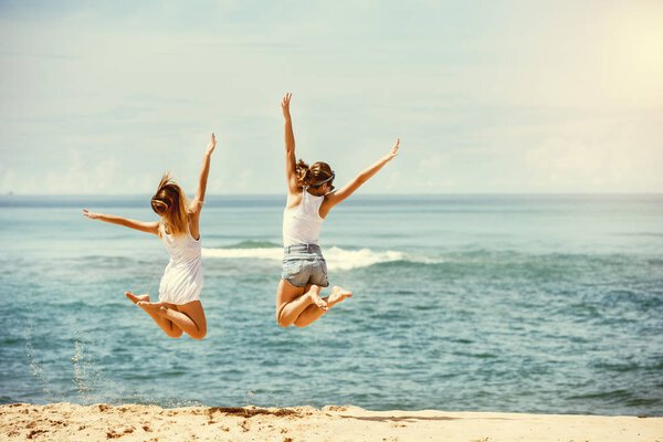 Two happy girls jumps at sunny beach