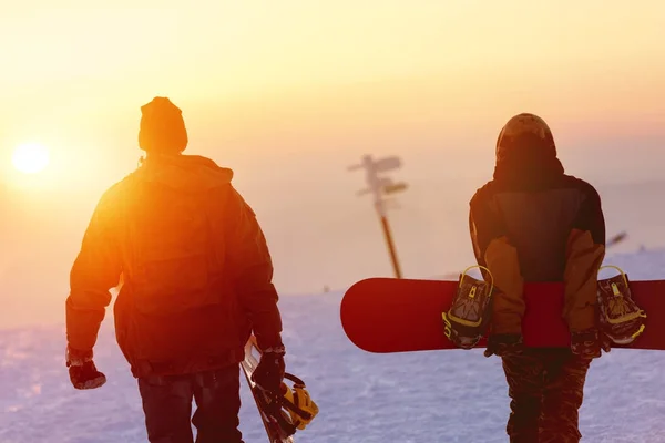 Dois snowboarders que andam de encontro ao céu do por do sol — Fotografia de Stock