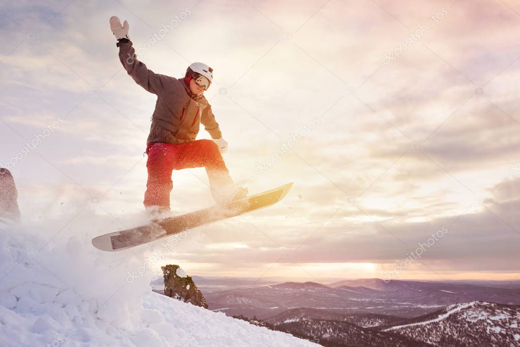 Snowboarder jumps against sunset sky