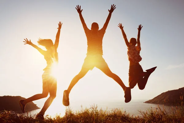 Glada vänner hoppar mot sunset sea bay — Stockfoto