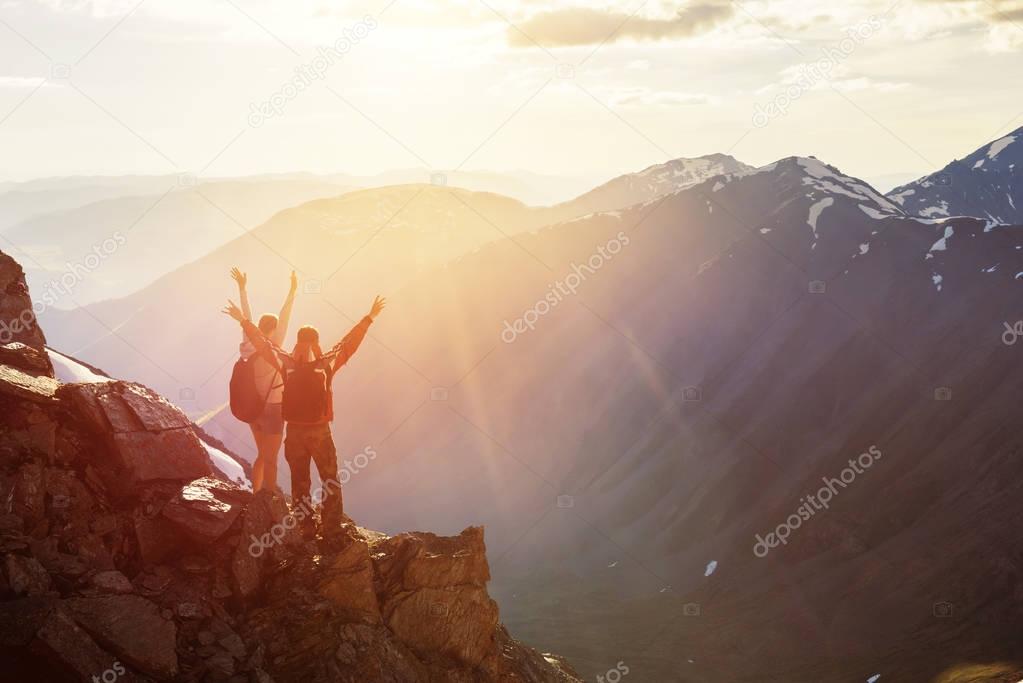 Two happy tourists greetings sunset with raised hands