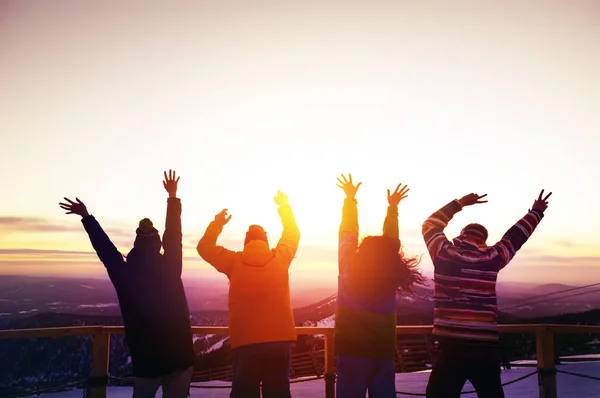 Amigos felizes com as mãos levantadas ao pôr do sol — Fotografia de Stock