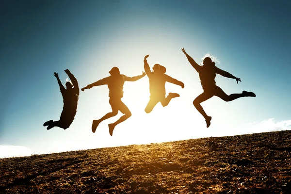 Four jumping silhouettes friends against sun — Stockfoto
