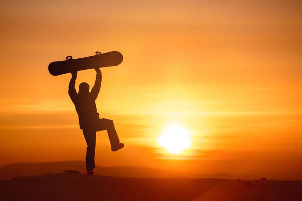 Happy snowboarder bailando con snowboard contra el atardecer — Foto de Stock