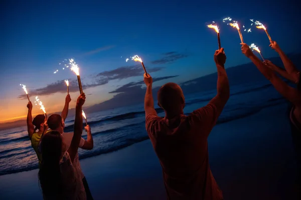 Amigos felices al atardecer fiesta en la playa con fuegos artificiales — Foto de Stock