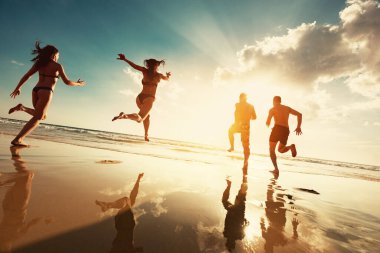 Mutlu turistler gün batımında deniz sahillerinde koşar