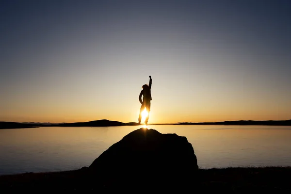 Homem salta em grande rocha contra o pôr do sol lago — Fotografia de Stock