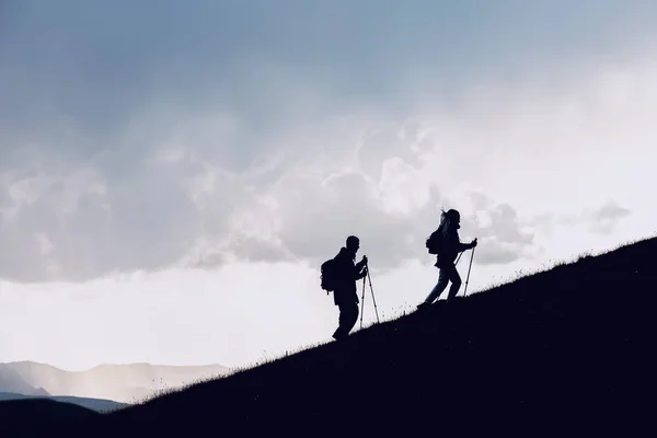 Duas silhuetas de caminhantes sobem as montanhas — Fotografia de Stock