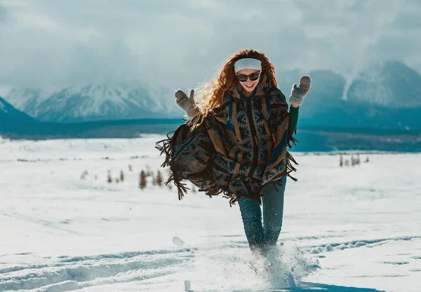Glückliches junges Mädchen im Poncho läuft im Schnee — Stockfoto