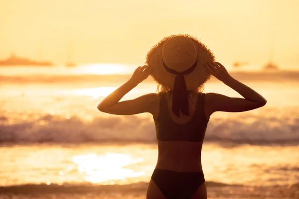 Beautiful slim girl with hat against sunset sea beach — Stock Photo, Image