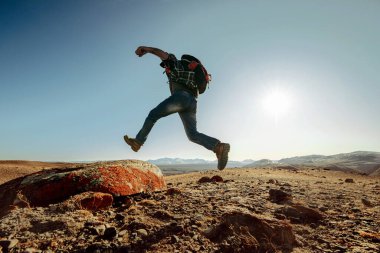 Sırt çantalı bir yürüyüşçü büyük kayaya atlıyor.