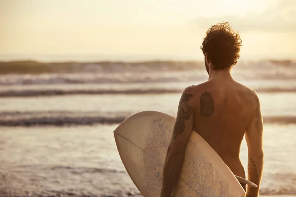 Atletisk surfare står med surfbräda vid solnedgången stranden — Stockfoto