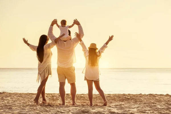 Família de quatro povos com braços erguidos na praia do pôr do sol — Fotografia de Stock