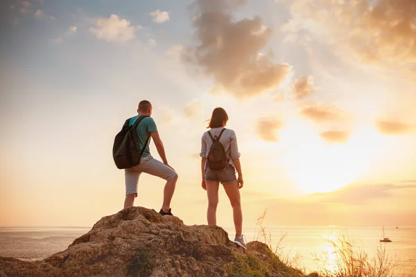 Twee wandelaars staat op grote rots en kijkt naar zonsondergang zee — Stockfoto