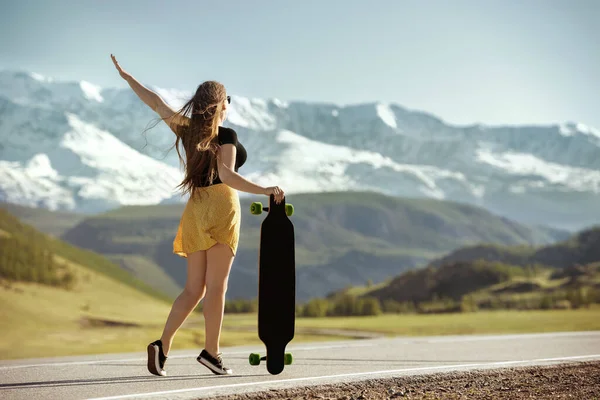 Menina com longboard está de pé na estrada da montanha — Fotografia de Stock