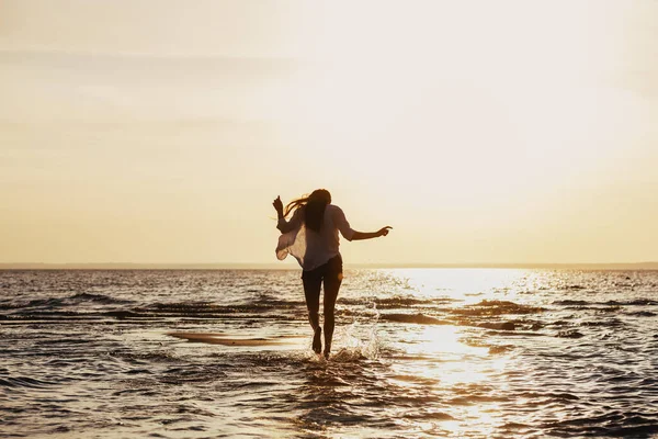 Schlankes Mädchen spaziert am Strand bei Sonnenuntergang im Wasser — Stockfoto