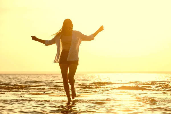 Menina bonita feliz caminha na praia do por do sol na água — Fotografia de Stock