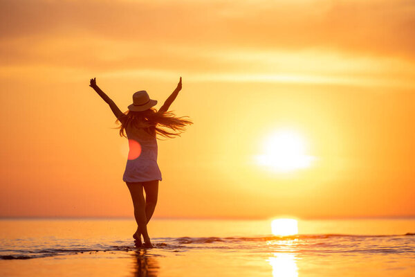 Young happy girl at sunset beach with raised arms