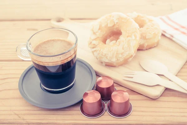 Cup of espresso and espresso capsule with bakery on wooden table.