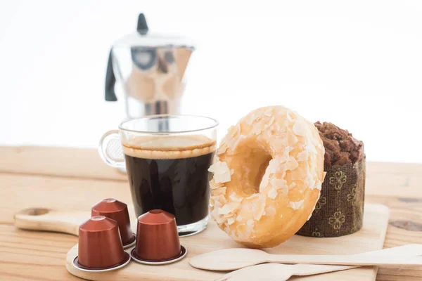 Cup of espresso and espresso capsule with bakery on wooden table.