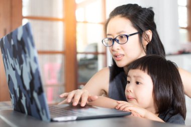 Asyalı bir kız annesiyle birlikte bilgisayardan online dersler öğreniyor ki bu gelecekte yeni bir normal olabilir. Covid-19 salgınında enfeksiyonu önlemek için..