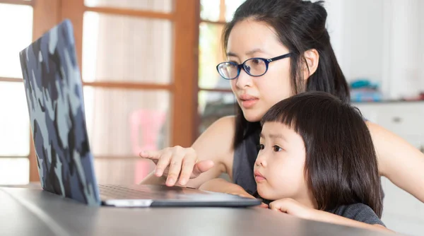 Asyalı bir kız annesiyle birlikte bilgisayardan online dersler öğreniyor ki bu gelecekte yeni bir normal olabilir. Covid-19 salgınında enfeksiyonu önlemek için..