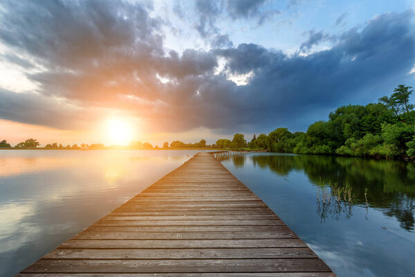 Wooden path bridge over lake at stormy dramatic sunset