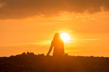 Genç kadının tek başına gün batımına doğru plajda yürüyor.